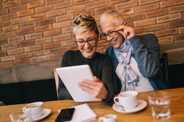 Wall Mural - Senior mother sitting in cafe bar or restaurant with her middle aged daughter and enjoying in conversation. 