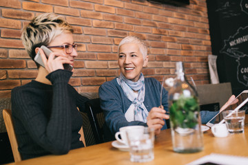 Wall Mural - Senior mother enjoying in cafe bar or restaurant with her middle aged daughter.