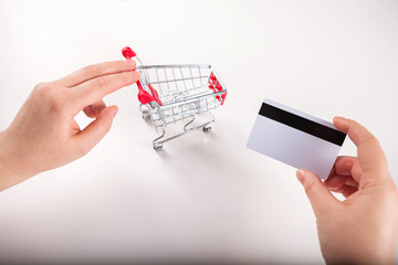 Woman forefinger pushing small shopping cart with Internet online shopping concept. Bank card nearby a laptop and mini shopping cart on white background top view.