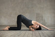 Young sporty woman practicing yoga, doing thread the needle exercise, spine bend pose, working out, wearing sportswear, black pants and top, indoor full length, gray wall in yoga studio, side view