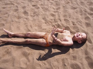 muddy boy lies on sand at the beach