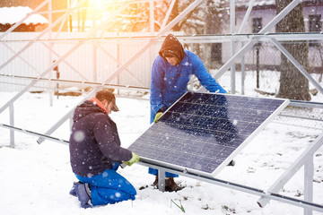 Two male electricians technicians workers installing solar panels outdoors in winter alternative electricity environment green friendly energy power photovoltaic station sustainable renewable.