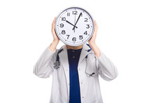 Young Woman Doctor With Stethoscope In Trouble Holding Clock In Front Of Her Head In White Uniform On White Background