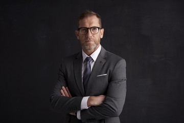 Executive senior businessman portrait. Middle aged financial director business man wearing suit and looking at camera while standing at dark background. 