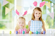 © MNStudio - Two cute little sisters wearing bunny ears playing egg hunt on Easter