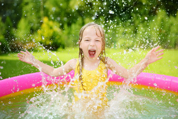 Sticker - Adorable little girl playing in inflatable baby pool. Happy kid splashing in colorful garden play center on hot summer day.