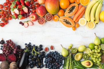 Healthy eating background, different varieties of colourful fruits and vegetables in rainbow colours on the off white table with copy space in the middle, top view, selective focus