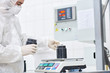 © Seventyfour - Confident factory worker wearing safety mask and coverall using electronic scale while filling in plastic bottle with sport supplement