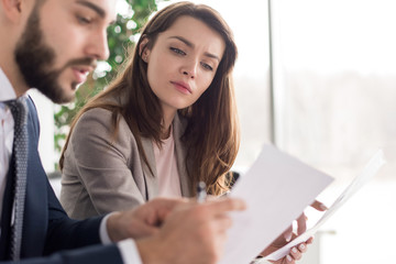 Wall Mural - Portrait of two modern business people discussing documents in office, focus on beautiful young woman reading text