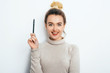 © victoriazarubina - Portrait of cheerful woman with appealing smile, having hair bun in sweater isolated on white background holding pen and have a great idea. Beautiful female showing emotions. People Beauty Fashion