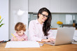 © baranq - Working mother concept. Young woman working on laptop with her child from home