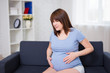 © Di Studio - pregnant woman getting a contraction at home in the living room