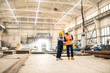 © Seventyfour - African American engineer wearing reflective vest and hardhat using digital tablet while discussing joint work with his colleague, interior of spacious production department of plant on background