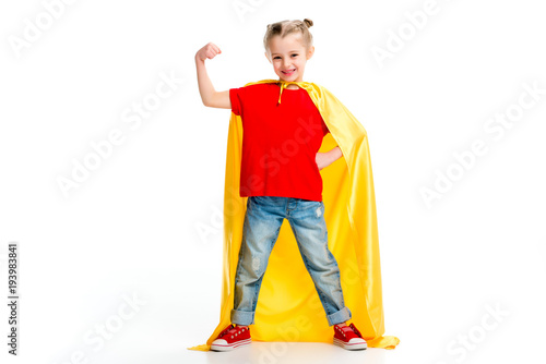 Photographie Smiling supergirl in yellow cape showing muscles on hand isolated on white