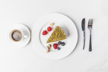 top view of sweet cake with pistachios and berries on plate and cup of coffee isolated on white