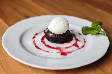 Wall Mural - A horizontal photo of a small brownie cake with vanilla ice cream, decorated with mint, strawberry sauce and cinnamon, served on a white plate.