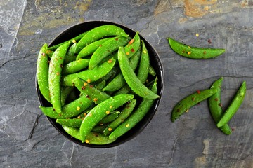 Bowl of healthy roasted snap peas. Top view over a dark slate background.