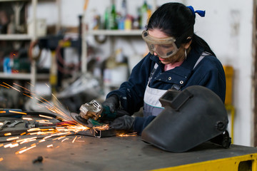 Wall Mural - Strong and worthy woman doing hard job in car and motorcycle repair shop. She using grinder to fix some metal bike parts.