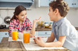 © zinkevych - Feeling inspired. Pretty happy little dark-haired girl smiling and talking with her brother while they having breakfast