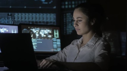 portrait of young woman programmer working at a computer in the data center filled with display screens