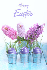 Wall Mural - Violet Easter eggs on a blue wooden table.Three colorfull egg in metal bucket.Flower hyacinth in bucket.Copy space.Easter background.Happy easter inscription