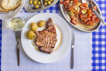 Wall Mural - Tuna steak accompanied with potatoes, olives, tomato salad, bread and wine