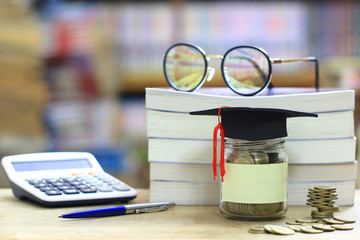 Graduation hat on the glass bottle on bookshelf in the library room background, Saving money for education concept