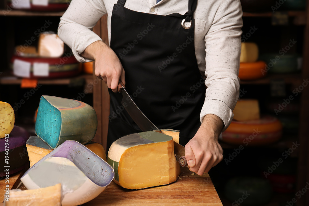 Young worker cutting cheese in shop