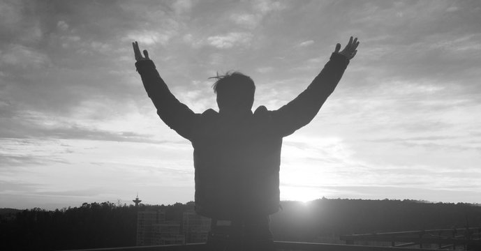 Praise and worship concept: Silhouette human raising hands to praying God on blurred cross with crown of throne sunset background