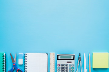 Calculator, notebook, pen, scissors and other office or school supplies on a table. Empty place for text on the blue background. Education concept. Flat lay.