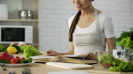 Wall Mural - Asian female reading ingredients list for salad in cooking book at home kitchen