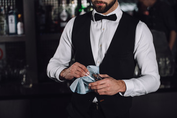 Wall Mural - cropped image of male bartender cleaning glass with rag in evening