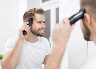 Handsome man cutting his own hair with a clipper