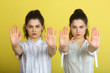 © Alexandr - two beautiful young girl sisters twins in white blouses on a yellow background with serious faces and gesture of hands
