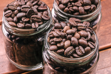 Roasted coffee beans in three glass jars on natural wooden boards.