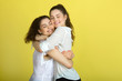 © Alexandr - two beautiful joyful sisters sister girls in white blouses on a yellow background hugging each other