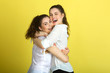 © Alexandr - two beautiful joyful sisters sister girls in white blouses on a yellow background hugging each other