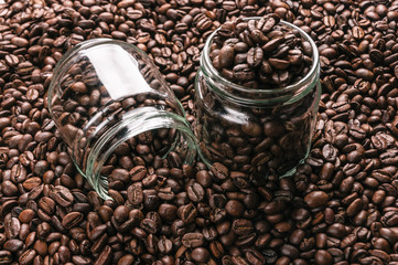 Two glass jars lie on roasted coffee beans.