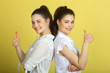 © Alexandr - two beautiful joyful sisters twin girls in white blouses on a yellow background showing gestures of hands a sign of success