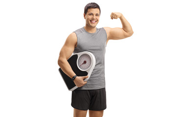 Sticker - Young guy in sportswear holding a weight scale and flexing his biceps