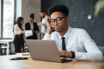 Poster - Tired young african businessman using laptop computer