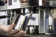 © svitlini - A barista at a cafe churns milk in a metal jug using a caper of  professional coffee machine. Coffee house concept. The process of making cappuccino or latte