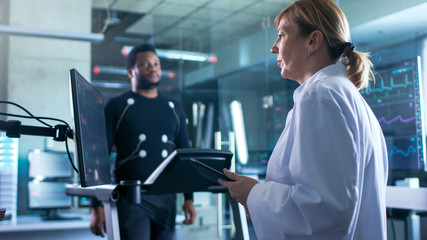 Wall Mural - sport scientist supervises reads ekg status while in the background male athlete walks on a treadmil