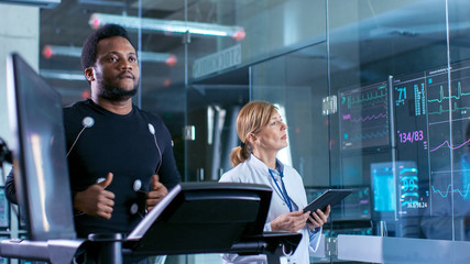 Wall Mural - male athlete runs on a treadmill with electrodes attached to his body while sport scientist supervis