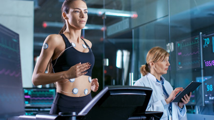Wall Mural - beautiful woman athlete runs on a treadmill with electrodes attached to her body, female physician u