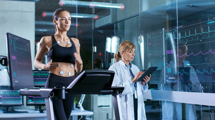 Wall Mural - beautiful woman athlete runs on a treadmill with electrodes attached to her body, female physician u