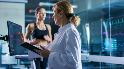 Wall Mural - sport scientist supervises touches display showing ekg status while in the background woman athlete 