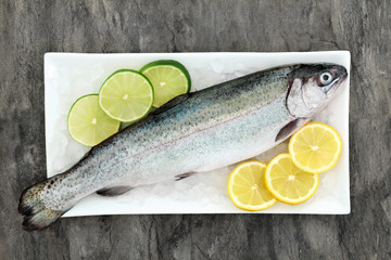 Rainbow trout health food on crushed ice with lemon and lime fruit on marble background. Very high in omega 3 fatty acid and beneficial to maintain a healthy heart.