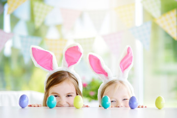 Wall Mural - Two cute little sisters wearing bunny ears playing egg hunt on Easter