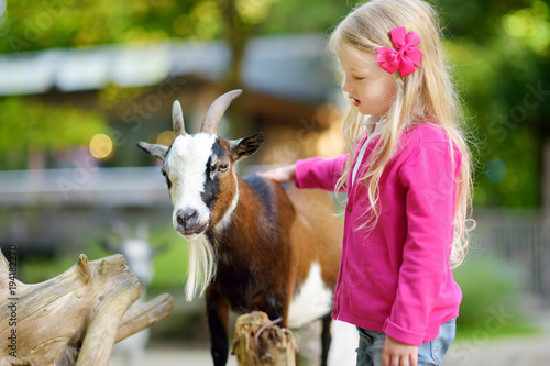 Fotografía Cute little girl petting and feeding a goat at petting zoo